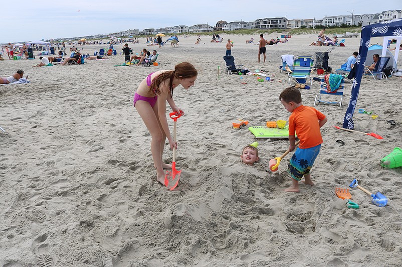 Billy Walker is buried in the sand by his cousin, Kasey Walker, and his little brother, Luke, during some fun time on the beach.