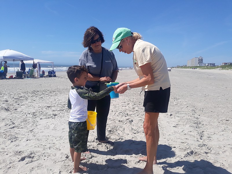 Liam McCollick, 5, hands a shell to beachcombing guide Carol Goldstein while his grandmother, Dee McCollick, watches.