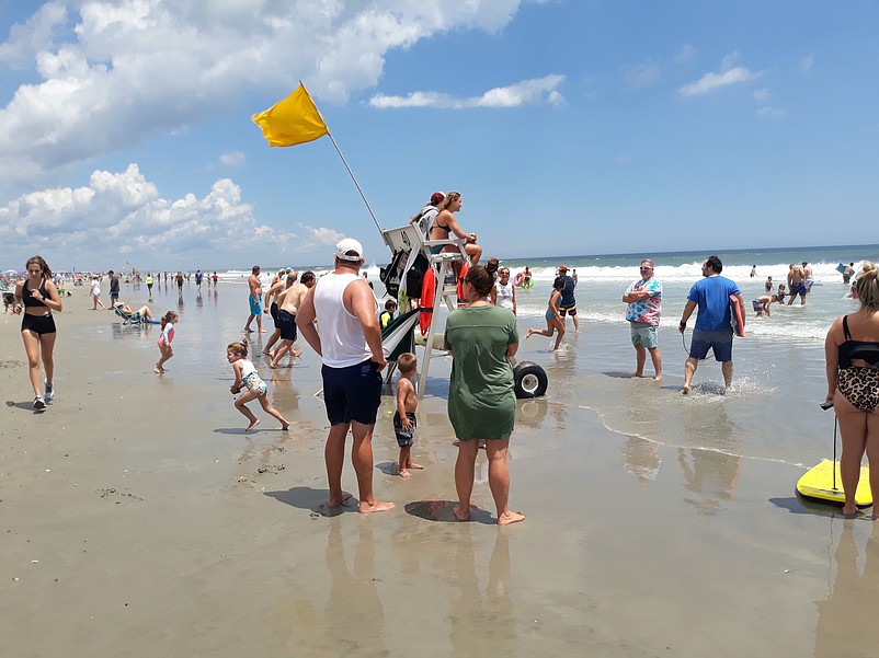 Beachgoers enjoy the water's edge, with a lifeguard nearby.