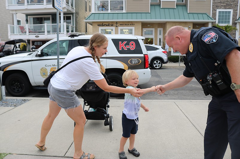 McQuillen fist-bumps with 3-year-old Conrad Dilks, while his mother, Abby Dilks, smiles during National Night Out, a community outreach event for the police department.