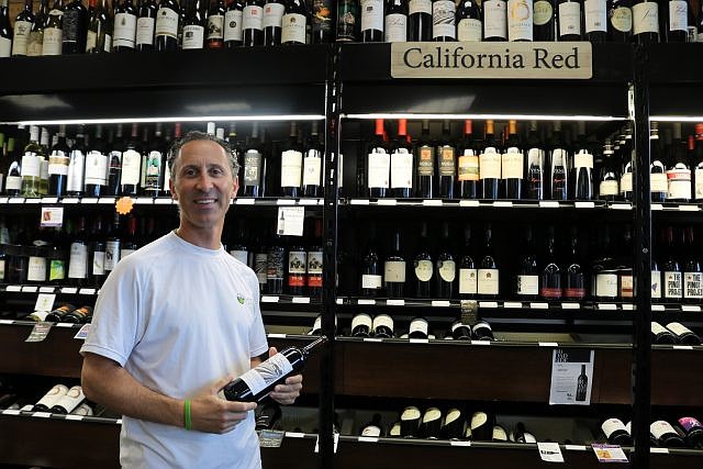 Passion Vines owner Michael Bray holds a bottle of red wine from an extensive collection of spirits.