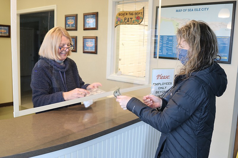 Sea Isle resident Suzanne Brindle hands money to JoAnn Kearney while buying eight beach tags for her family.
