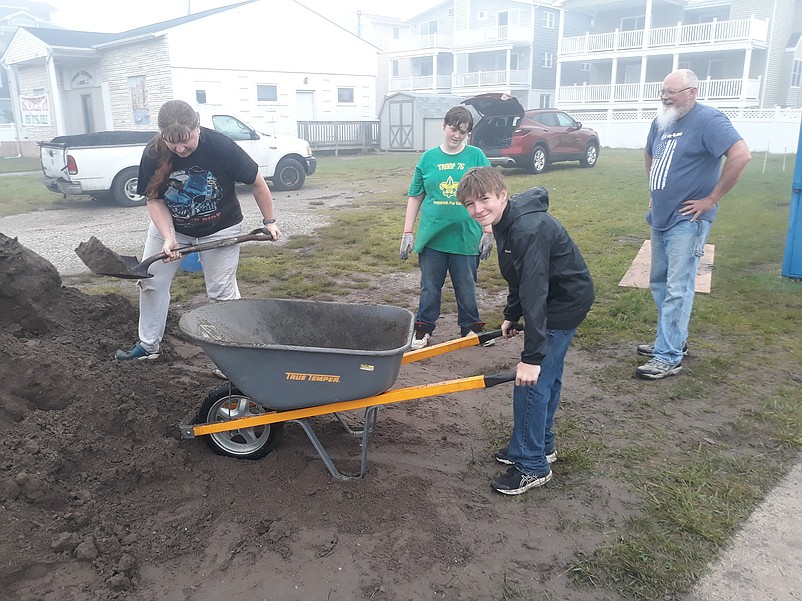 Boy Scout Benjamin Banks holds the wheelbarrow while Beth Rivello, whose son, Aiden, is a Boy Scout, shovels some garden mulch.