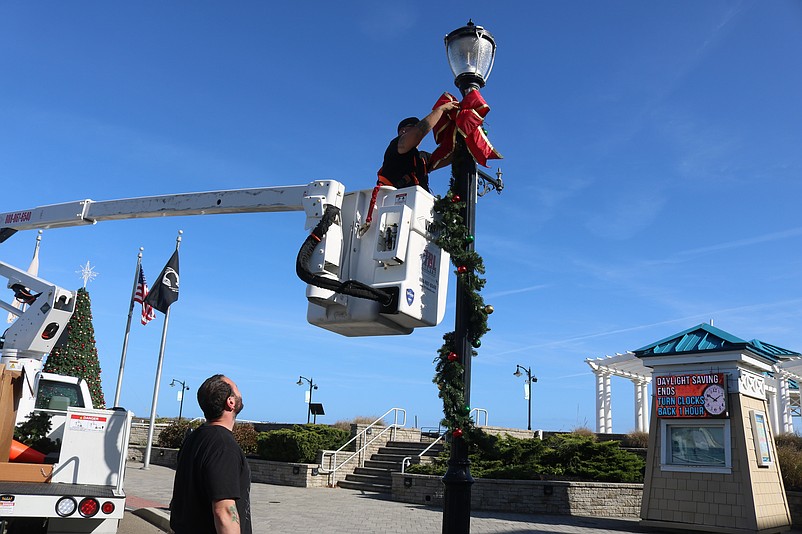 Rileighs Outdoor Decor workers Jake Bjorbekk, in lift, and Frank Capozzi hang holiday bows and garland on street lamps.