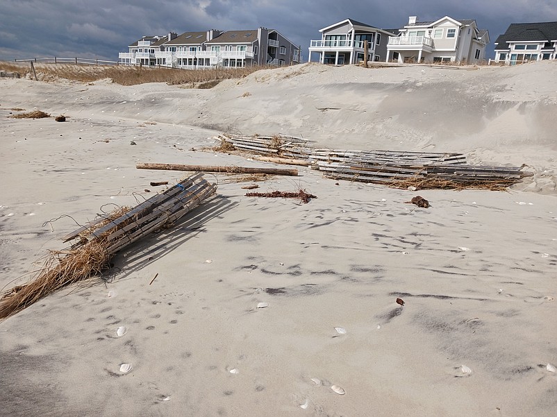 A destroyed section of dune fencing and other debris litter the beach.