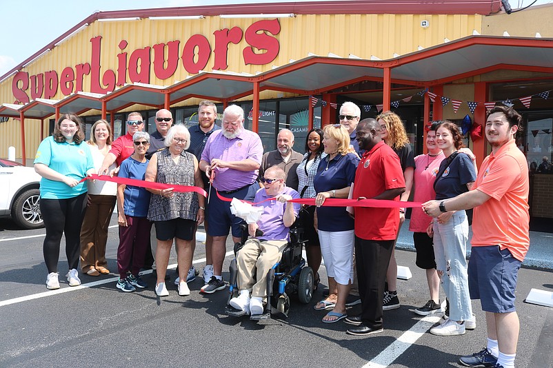 Joined by dignitaries, employees and family members, Super Liquors' third-generation owner Dave Beyel Sr. uses a pair of oversized scissors to cut the ceremonial ribbon.