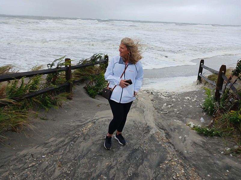 Kelly Lawson stands on a beach pathway as big waves wash away the sand.