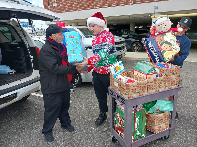 Joseph Rutledge, center, hands a package to Mayor Leonard Desiderio, while Rich Seib takes a present off the gift cart during the 2023 toy and food drive.