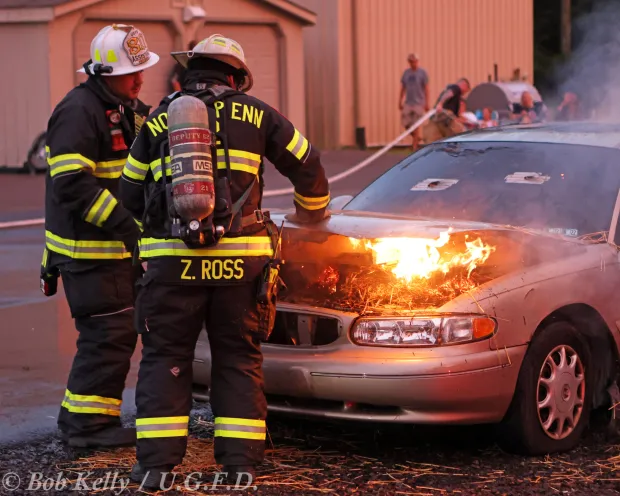 An Upper Gwynedd Fire Department, left, and a North Penn Volunteer Fire Company firefighter work together on a car fire. (Photo by Bob Kelly for UGFD)