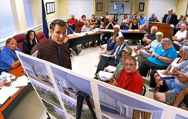 Matt Bartelt, owner of the Trego House, left, with his attorney Ed Hughes, back right standing, explains photos of the house he refurbished to the North Wales Borough Zoning Hearing Board along with a packed room of residents during a meeting Sept. 1. Mark C. Psoras - Montgomery Media
