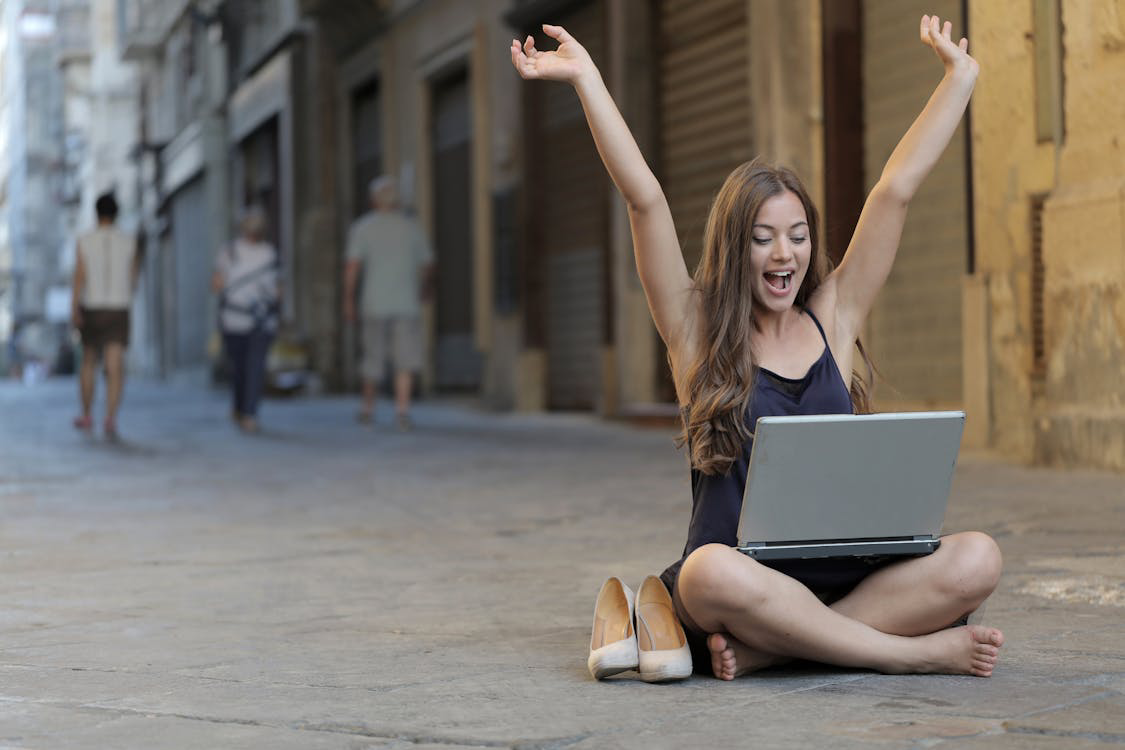 Free Woman Raising Her Hands Up While Sitting on Floor With Macbook Pro on Lap Stock Photo