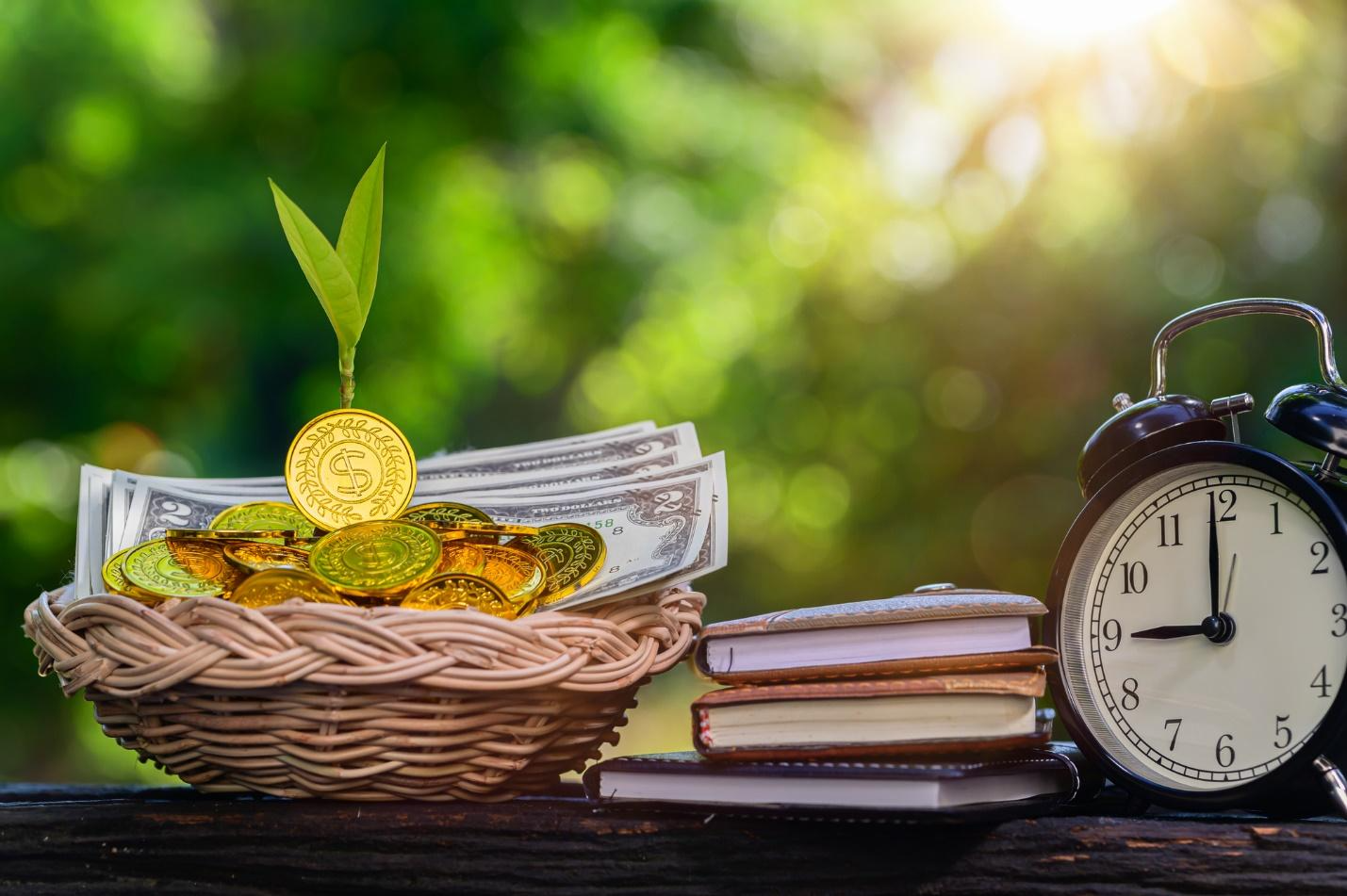 A basket of gold coins and money next to a clock 
Description automatically generated