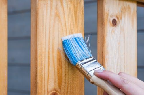 Free A hand painting a wooden fence plank with a blue paintbrush outdoors. Perfect for DIY and renovation themes. Stock Photo