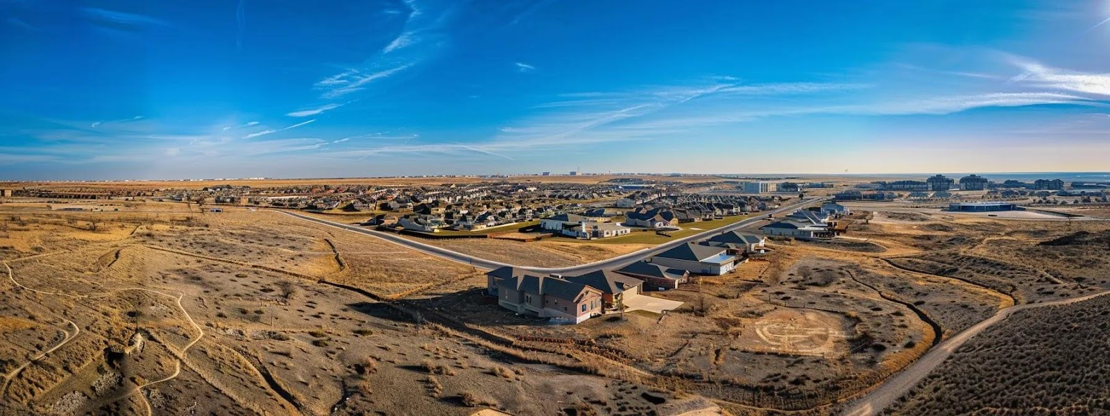 an expansive, sprawling desert landscape dotted with modern homes and commercial buildings under a bright blue sky, showcasing the lucrative investment potential of lubbock, texas real estate.