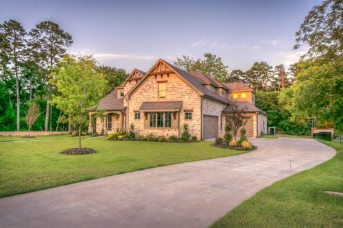 Free Elegant stone family home surrounded by trees, lush lawn, and vibrant garden. Stock Photo