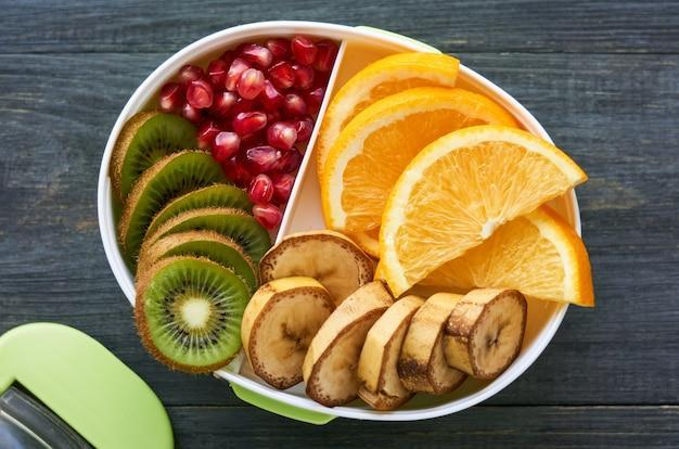 Lunch box with various fresh fruits on wood