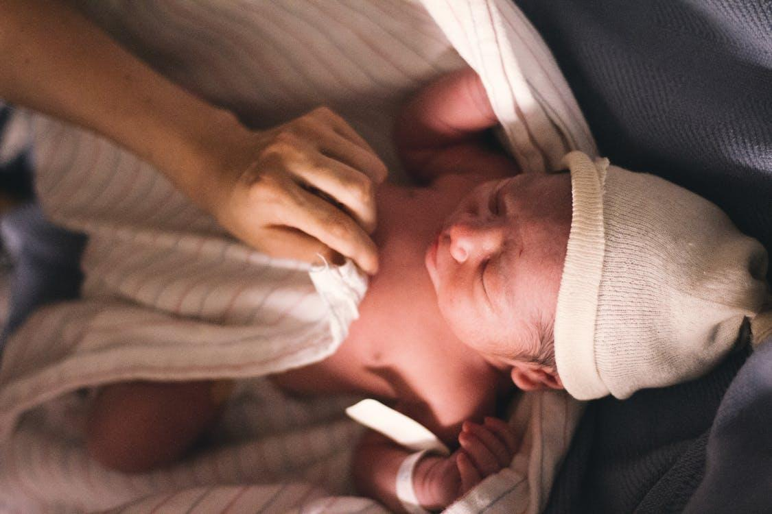 Free A serene moment of a newborn baby swaddled in blankets with a tender touch of a parent's hand. Stock Photo