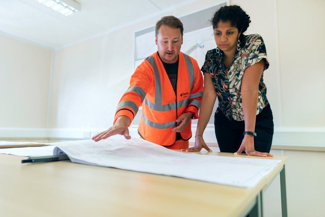 Free Two engineers reviewing blueprints in an office, discussing project details. Stock Photo
