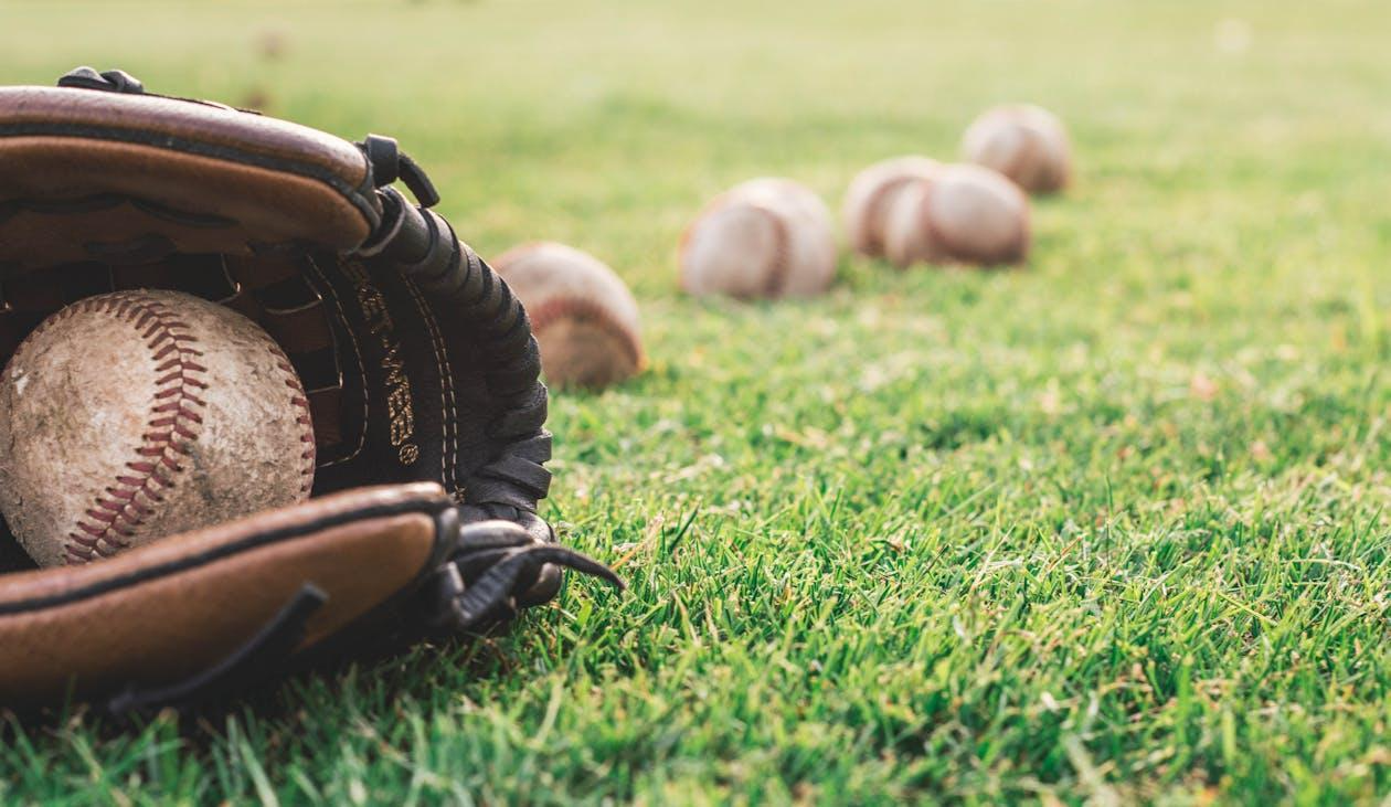 Free A close-up of a baseball glove with balls on a green field, symbolizing outdoor sports. Stock Photo