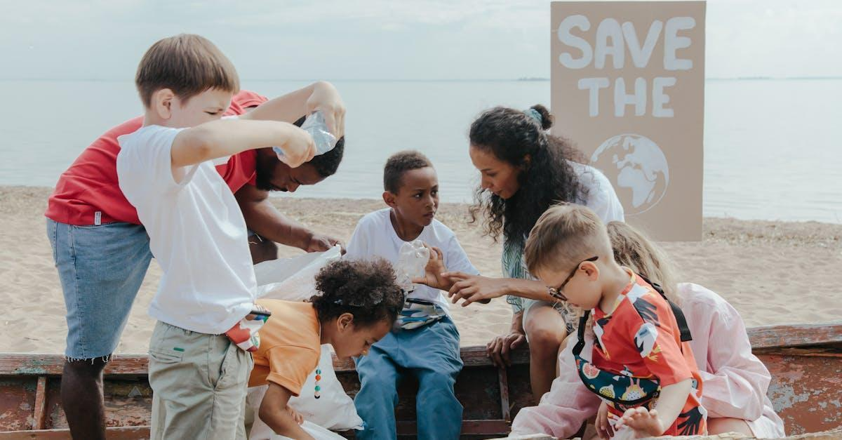 A group of children volunteering to clean a beach with a 'Save the Earth' sign.