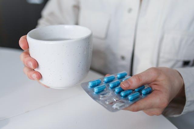 A person holding a mug and blue pills
