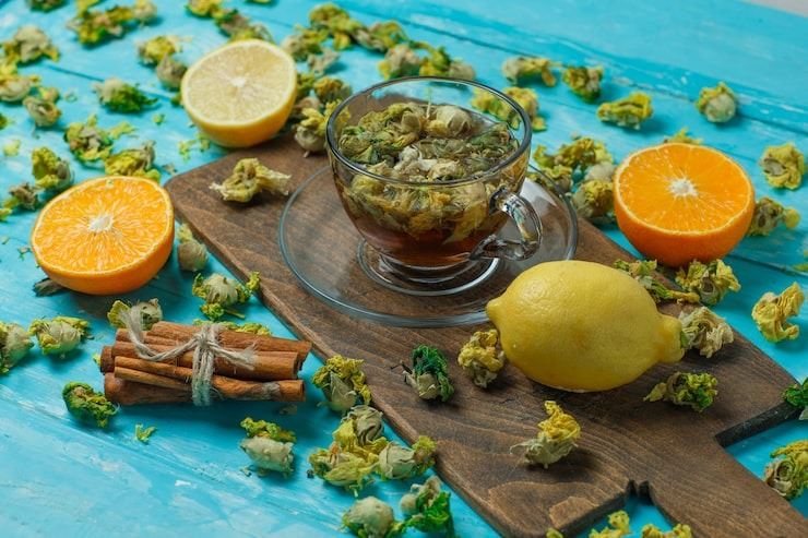 tea with spices, orange, lemon, dried herbs in a mug on blue and cutting board, high angle view.