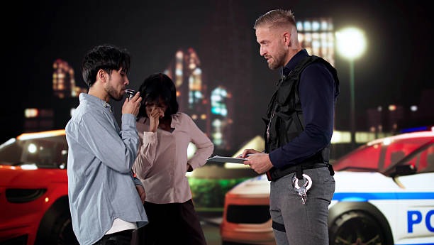 Driver Taking Breathalyzer Test As Passenger Watches With Concern Driver Taking Breathalyzer Test As Passenger Watches With Concern At Checkpoint. DUI Defense  stock pictures, royalty-free photos & images