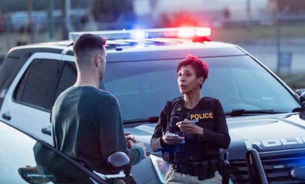 Policewoman taking a statement from young man A policewoman taking a statement from a civilian outside her patrol car. The officer is a mature African-American woman in her 40s. She is talking with a young man in his 20s. witness statement stock pictures, royalty-free photos & images
